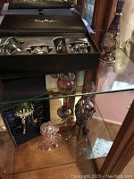 Photo of various perfume bottles including pink glass bottle, two tall metal stand bottles in red and clear glass, and boxed Thierry Mugler set