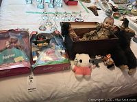 Lot overview showing boxed Barbie dolls, vintage baby doll in wooden box, plush moose, Ty Beanie toys, and various small figures arranged on a bed