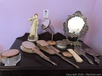 Full view of vintage vanity brushes, hand mirrors, silver-plated standing mirror, and Roberto Brambilla figurine on wooden base.