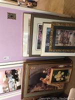 Wide view of the stacked framed prints against a pink wall, showing a variety of frames and sizes.