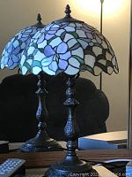 Photo of a 22 inch Tiffany style stained glass table lamp with purple and blue floral pattern shade and ornate metal base.