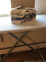 Ironing board with striped cover and folded metal X-leg frame; Hamilton Beach electronic iron in original box placed on board