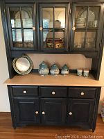 Black painted solid wood dining room hutch with three glass-front upper cabinet doors and six lower drawers and doors. Lighted top section visible.