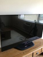 LG 55-inch flat screen TV shown angled on a wooden surface, reflecting window blinds and room interior.