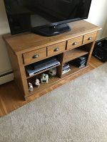 Photo of a solid oak TV stand with three drawers on top and divided open shelves below, TV partially visible on top.
