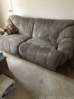 Photo of a large gray microfiber double reclining sofa with throw pillow on the left side, placed against a white wall