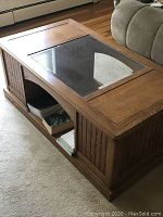 Photo shows the solid oak coffee table with glass top and inside storage compartments, placed on a carpeted floor near a sofa.