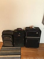 Photo showing three pieces of assorted luggage, all soft-sided with wheels and extendable handles. Colors vary in black and gray shades with multiple front zippered pockets.