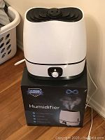 White ultrasonic humidifier sitting on its original box in a home setting.