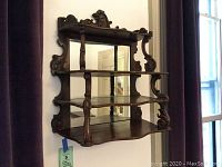 Front view of the ornate wooden wall shelf with mirrored back, showing three shelves, intricate carved detailing, and curved shelf edges.