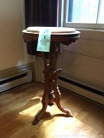 Full view of the round wooden table/plant stand with carved legs and marble inset top.