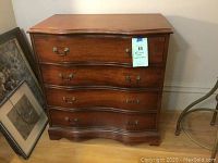 Front view of the serpentine front chest showing four drawers with brass bail pull handles and keyhole escutcheons.