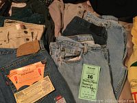 Multiple pairs of Levi's button fly jeans in various colors and washes including beige, green, blue, black with original labels and tags