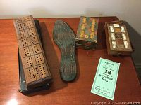 Four vintage cribbage sets displayed on a wooden surface showing a wooden board, shoe last board, and two other boards including a box with a game card.