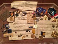 Top down photo showing the whole lot with medals, ribbons, pins, patches and various military documents arranged together on wood surface.