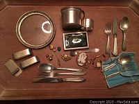 Overhead shot of entire lot on wooden tray showing plate, napkin rings, cups, card case, flatware, and jewelry.