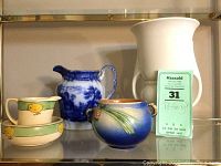 Shelf display showing four pottery items: two baby chick pieces, a blue and white pitcher, and a blue vase.
