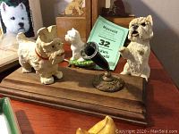 Photo of multiple Westie dog figurines including resin dogs on wooden base with small gramophone figure