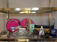 Wide view of many items including Royal Albert teacup and saucer set, decorative Dr. Johnson tin, porcelain figurine, and apple-shaped item on a glass shelf.