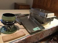 Photo showing green fondue pot on heating stand, rectangular serving tray, and stainless steel chafing dish with lid and stand.