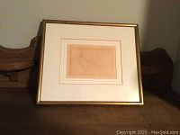 Overall view of first framed print showing beige toned line drawing of reclining nude, double mat and gold frame