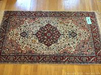 Full view of rectangular vintage oriental area rug on hardwood floor, showing entire pattern, colors, and fringed edges.