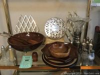 Photo showing the large wooden bowl with wooden salad servers, silverplate salt and pepper shakers, silverplate trivets, glass vase with silverplate holder, and additional wooden plates and bowls arranged on a glass shelf.