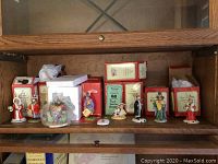 Seven figurines on wooden shelf with red and yellow Royal Doulton Bunnykins boxes behind