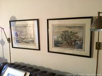 Wide shot of two framed hunting scene prints on wall above couch showing size and framing.