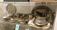 Shelf with assortment of silverplate serving pieces including trays, pitchers, utensils, and covered items
