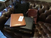 All items grouped on a couch: black hard briefcase, vintage brown leather shoulder bag, brown leather folio organizer, black nylon laptop sleeve bag