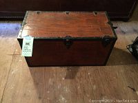 Full front view of the wooden trunk with metal trim and blue sale tag attached.
