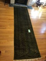 Full view of mossy green oriental runner rug laid out on wood floor; shows length and pattern detail.