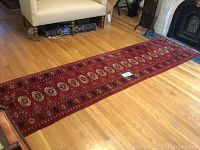 Full length of the russet red oriental runner in a room with wood flooring and furniture for scale showing the overall pattern and condition.