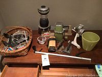 Photo showing various kitchen and household items arranged on a wooden surface including Kosta Boda bowl, ice crusher, meat grinder, scale, flashlight, and green bowl.