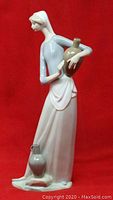 Front view of the Lladro figurine showing the girl holding a tan jug with a smaller gray jug on the ground, set against a red background.