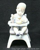Front view of Lladro figurine showing child in high chair holding yellow rubber duck.