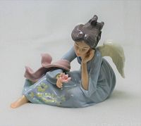 Front view of the angel figurine sitting with flowers, showing facial features and hand holding a flower.