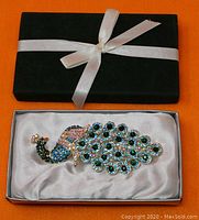 Closed black box with a silver ribbon on an orange surface; contains the jewelry presentation box inside.