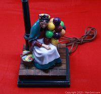 Front view of the Balloon Lady ceramic lamp showing the figurine and wooden base with tiled detail and lamp post.