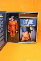 G.I. Joe Action Pilot figure in orange flight suit displayed in original box next to an illustrated history book titled 'GI Joe The Story Behind the Legend'.