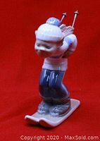Side angle view of Lladró skier puppet figurine showing blue and white glazed porcelain with ski boots on skis and ski poles strapped on the back.