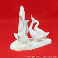 Side view of glossy white porcelain figurine showing three geese around a tree stump with smooth finish on red background.