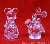 Front view of clear lead crystal Minnie Mouse dressed figure and Mickey Mouse holding hat salt and pepper shakers on red background.