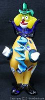 Front view of the colorful Murano glass clown figurine showing yellow body, large blue collar, red lips, white gloves, and black feet.
