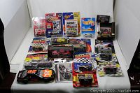 Photo showing a wide assortment of Nascar diecast cars including several in original packaging from brands like Winners Circle and loose cars in front, including a black and orange number 28 car.