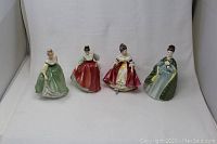 Four Royal Doulton porcelain figurines displayed on a white background, showing full figures including dresses and hairstyles.
