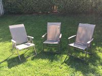 Three outdoor folding chairs set up on grass showing front and side views, highlighting mesh material and armrests.