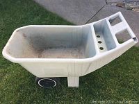Full side view of the gray plastic AMES Easy Roller lawn cart resting on grass, showing basin, wheels and handle.