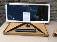 Front view of the black tempered glass shelf laying on cardboard box with included mounting brackets and wire spine below it